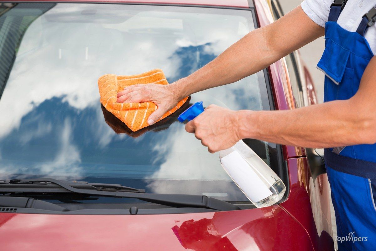 Main nettoyant le pare-brise d'une voiture rouge avec un chiffon et du nettoyant pour vitres